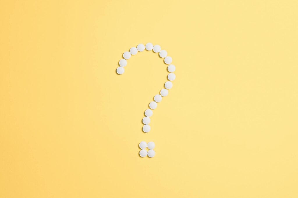 White pills arranged into a question mark shape on a vibrant yellow background.